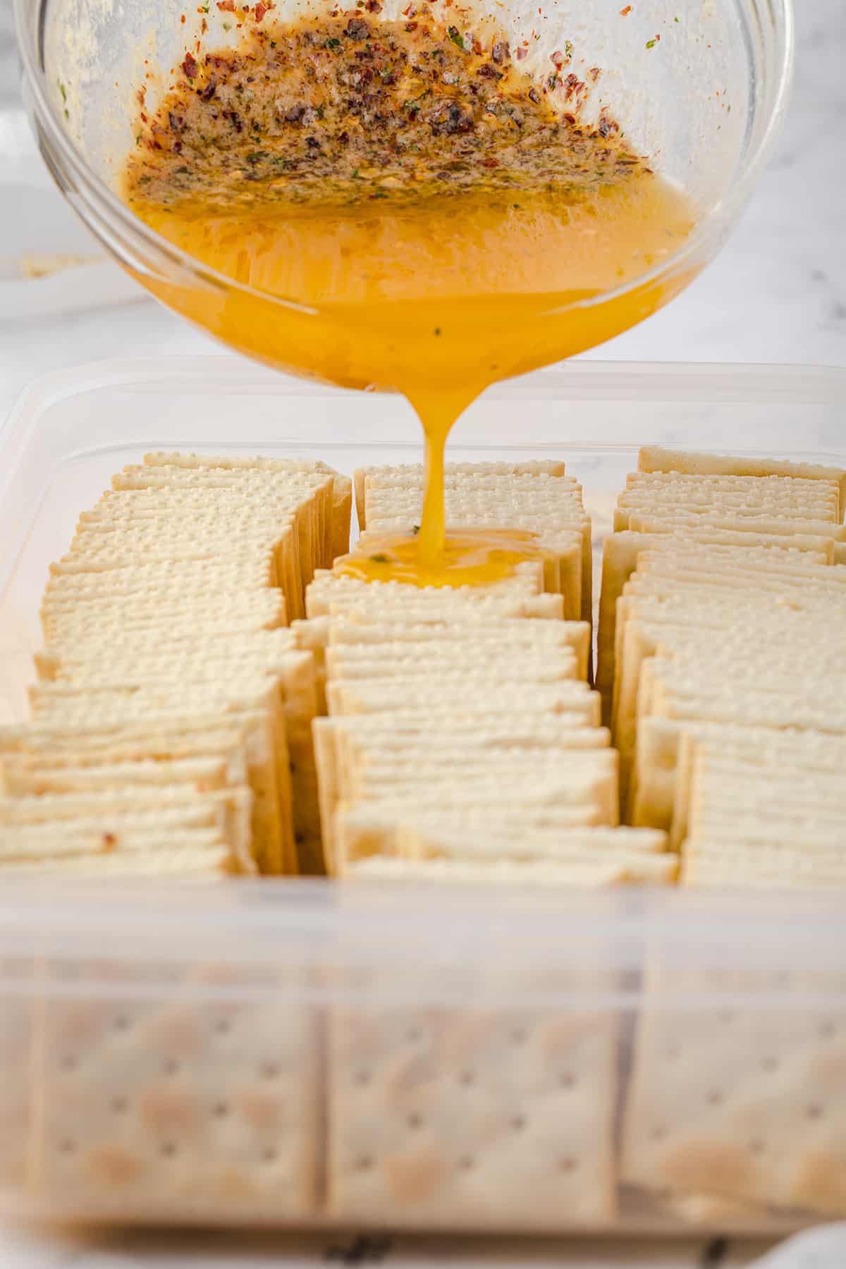 Pouring butter-spice mixture over crackers.