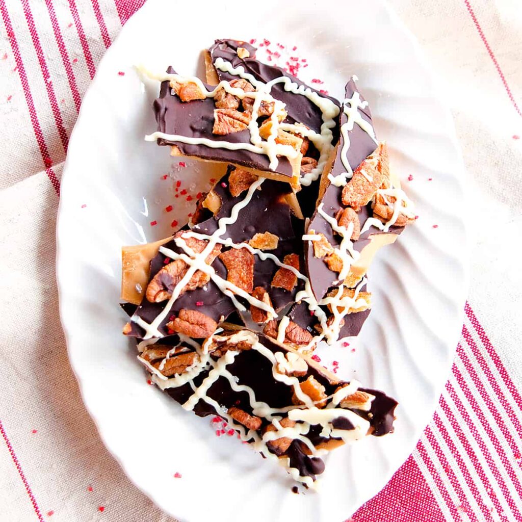 Pieces of bacon and pecan topped toffee on a serving plate.