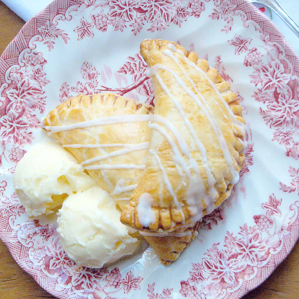 Two apple hand pies with vanilla ice cream on a serving plate.