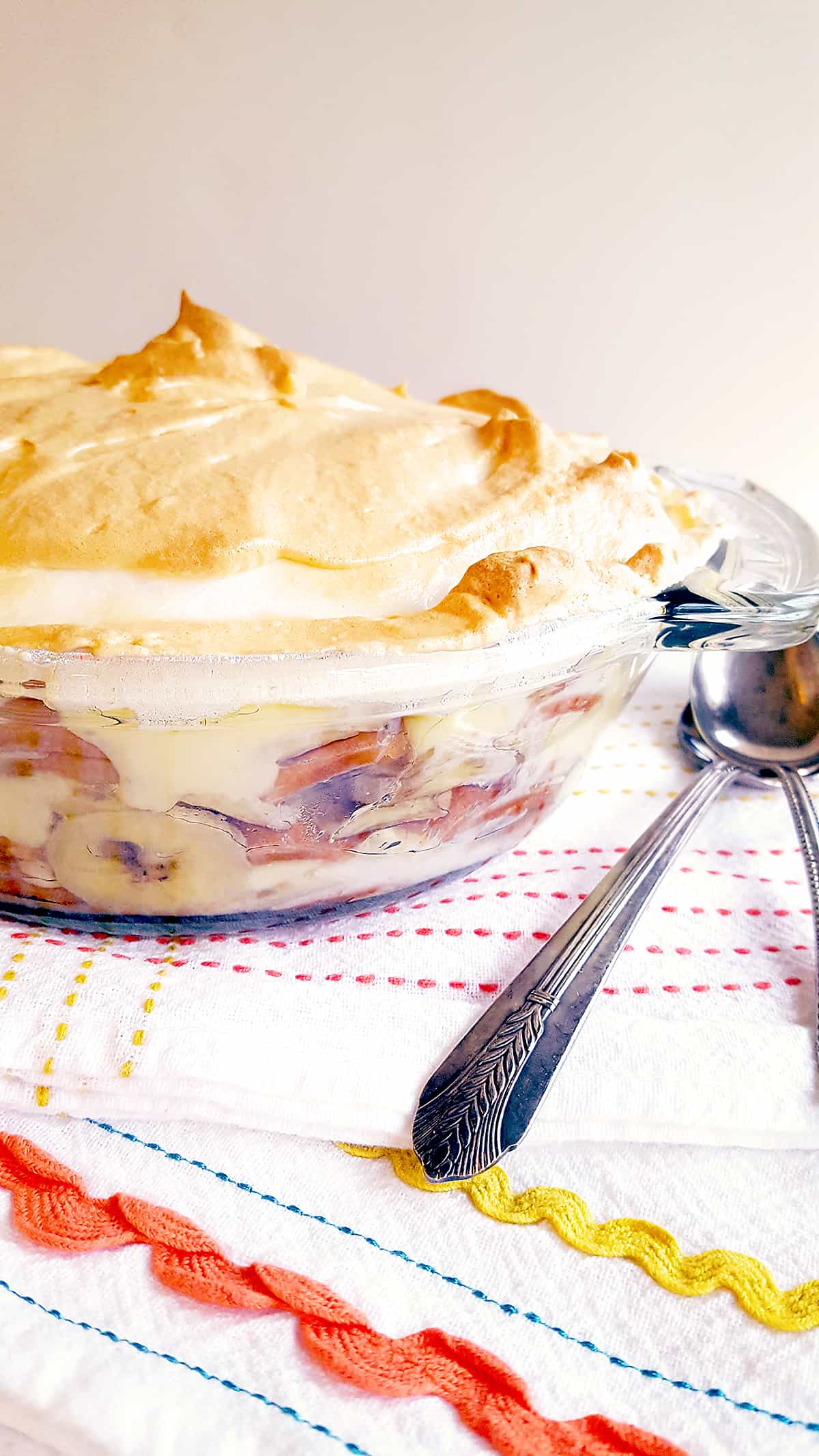 Finished banana pudding in a bowl with a kitchen towel and spoons in the foreground.