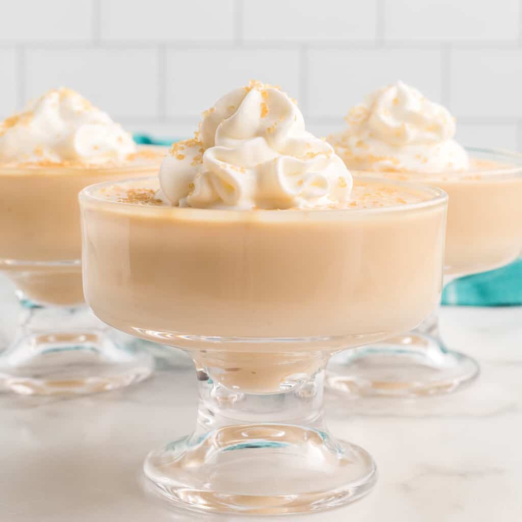 Three dishes filled with butterscotch pudding topped with whipped cream and turbinado sugar.