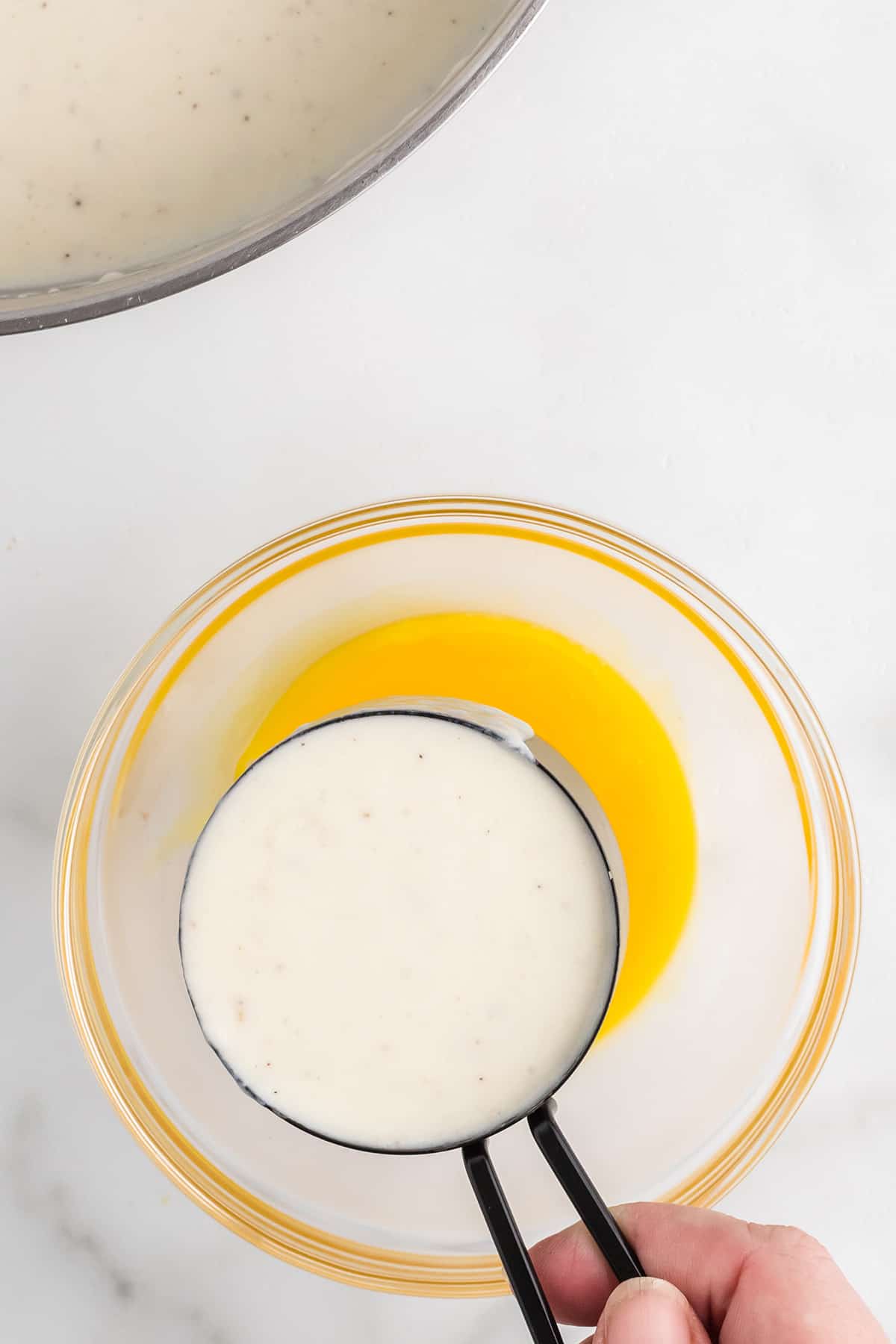 Adding hot mixture into egg yolks.