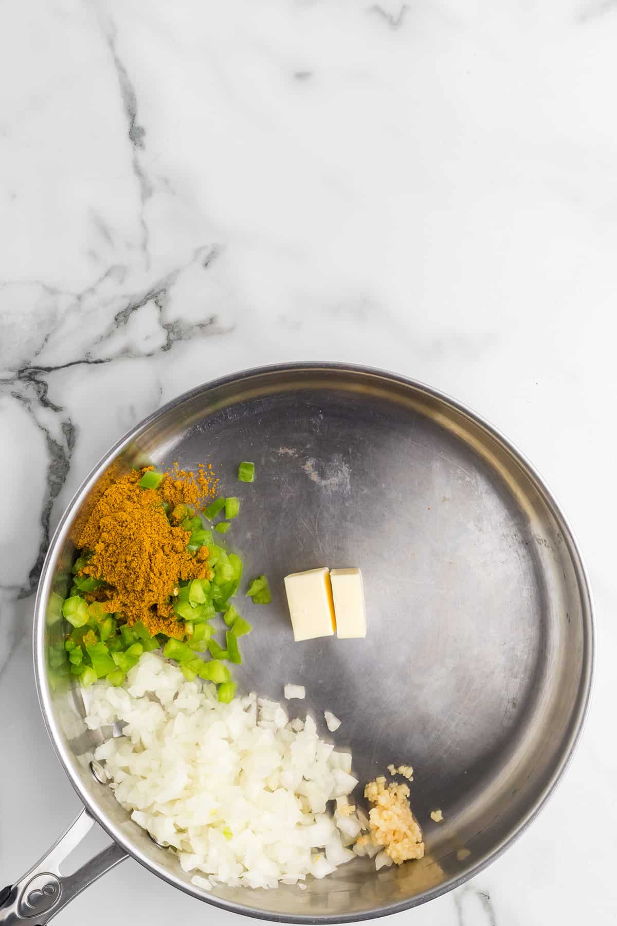 Butter with onions, peppers, garlic, and curry powder in a frying pan.