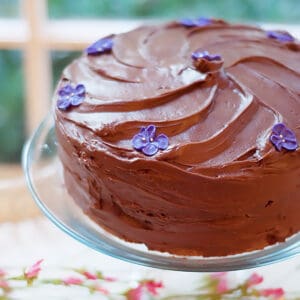 Finished cake decorated with sugar violets on a pedestal.