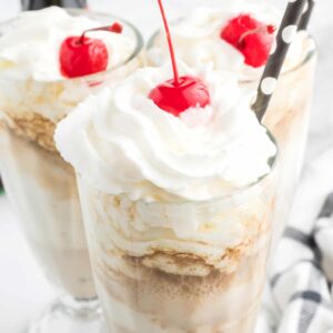 Coke floats in tall glasses with whipped cream and a cherry on top.