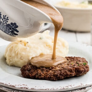 Gravy being poured onto country fried steak on a plate with mashed potatoes.