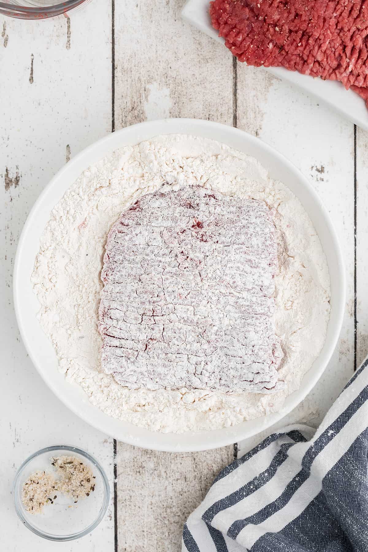 Dredged steak sitting on top of flour.