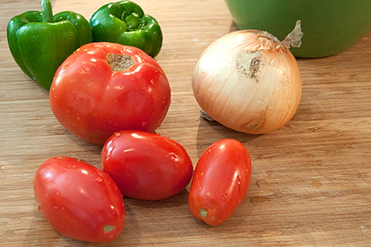 Tomatoes, onions, and peppers on a cutting board.