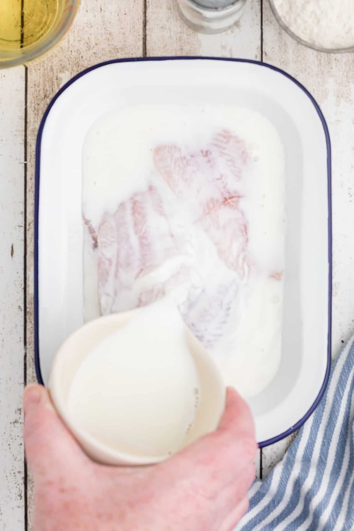 Pouring milk over catfish fillets in a pan.