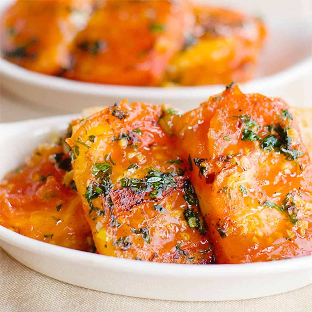 Garlic fried tomatoes in a small white serving bowl.