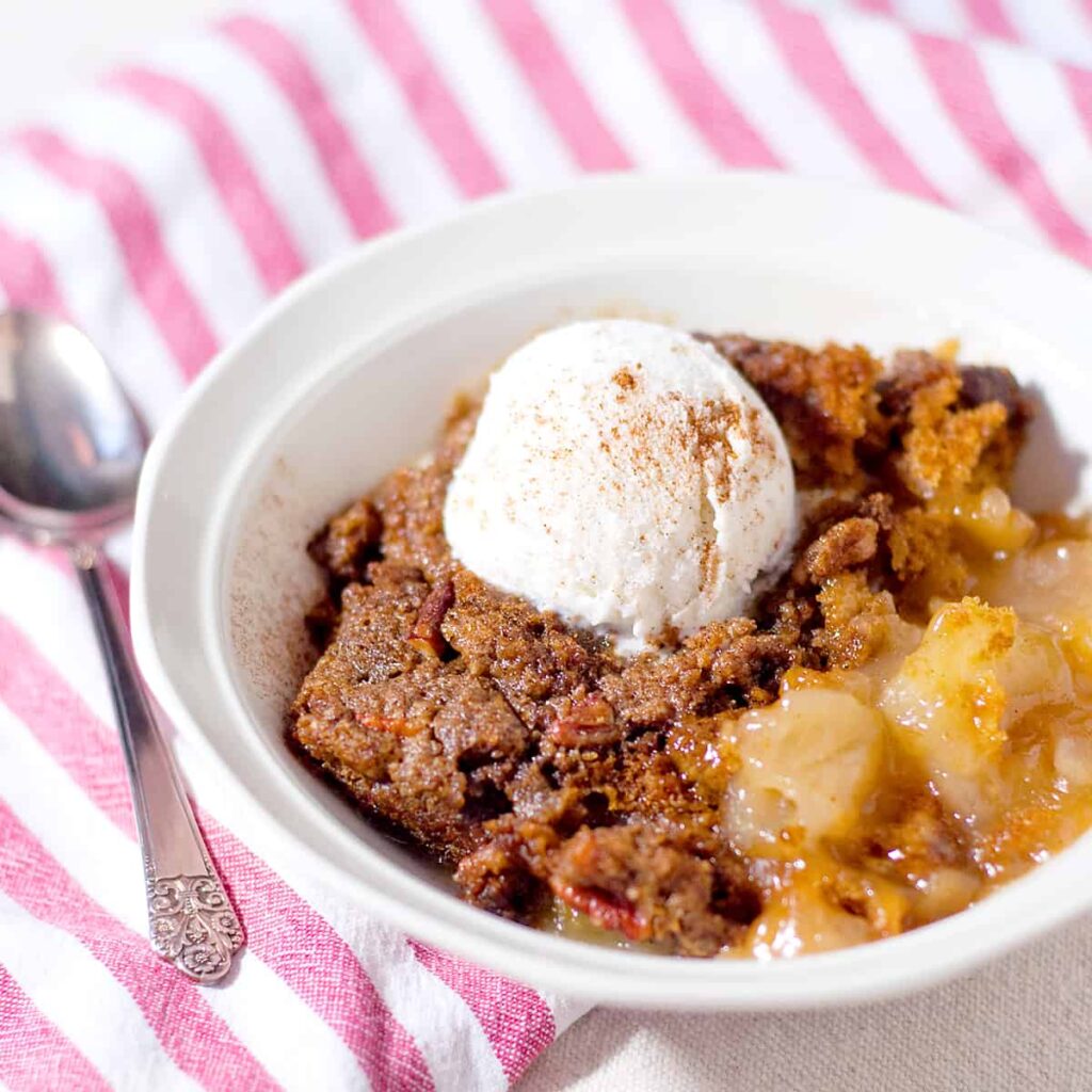 A white serving bowl filled with cobbler and a scoop of vanilla ice cream.