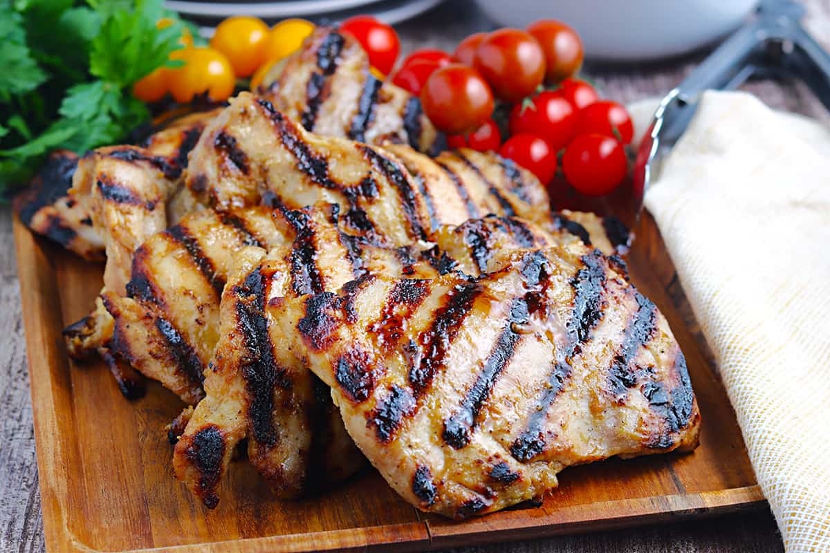 Finished grilled chicken thighs on a wooden board.