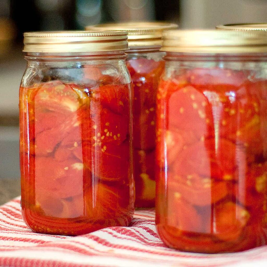 Jars of home canned tomatoes sitting on a kitchen towel.