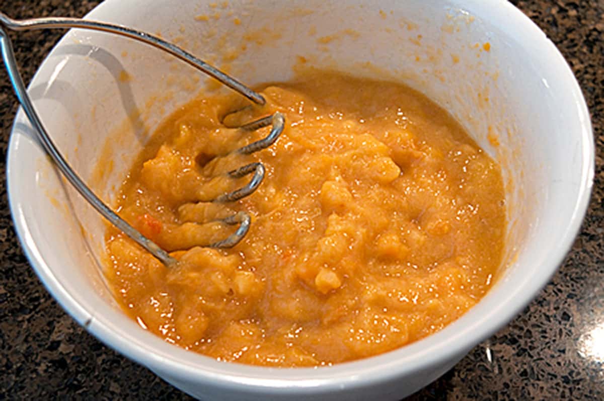 Fresh ripe peaches being mashed in a mixing bowl.