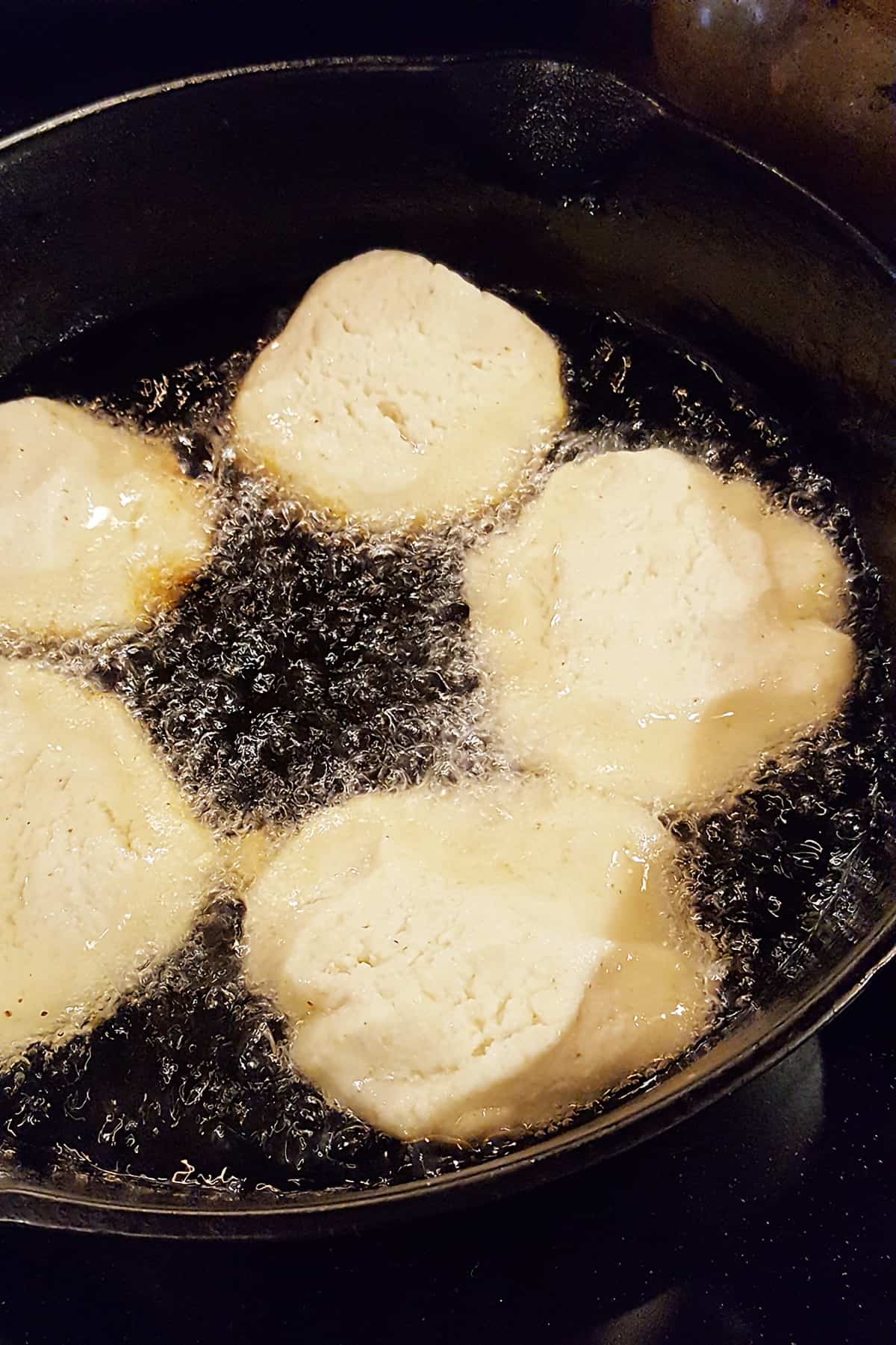 Cornbread patties placed in hot oil in a cast iron skillet.