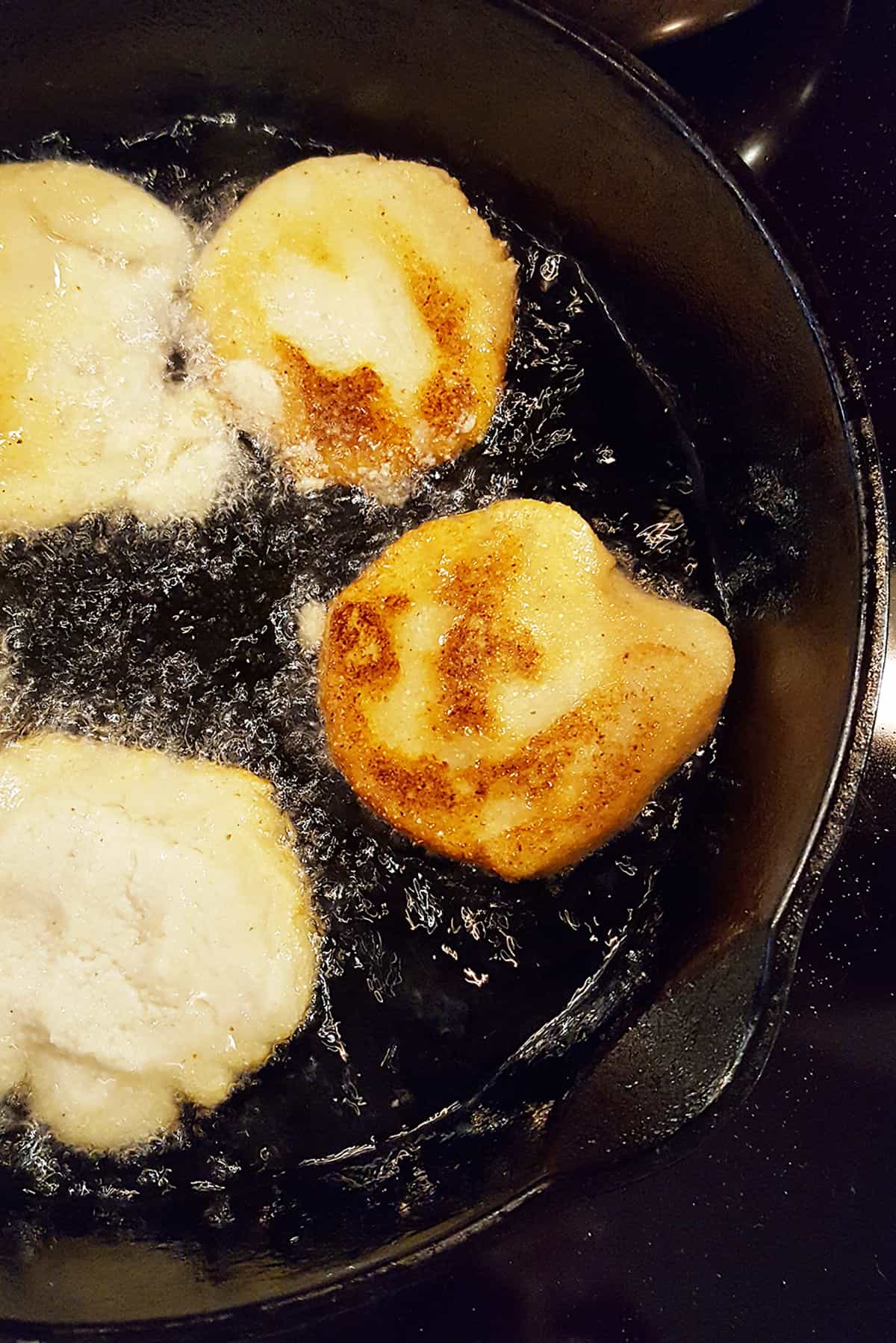 Cornmeal patties in a cast iron skillet after browning on the first side.