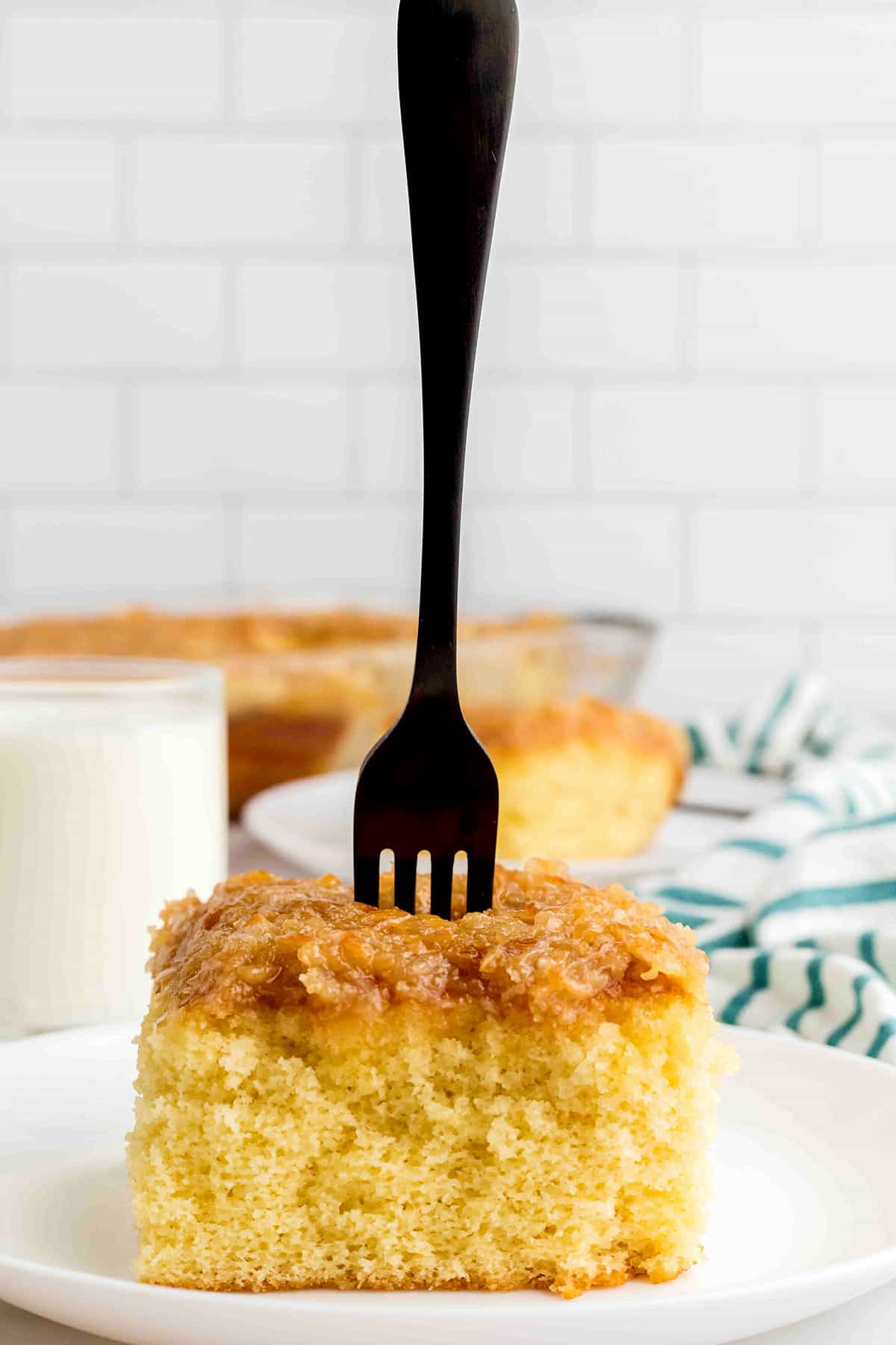 A slice of cake on a plate with a fork standing upright.