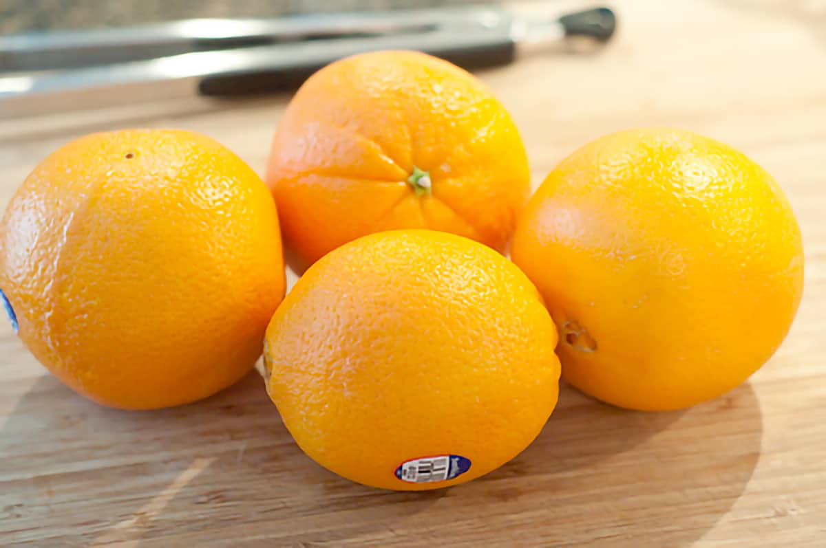 Four navel oranges on a cutting board.