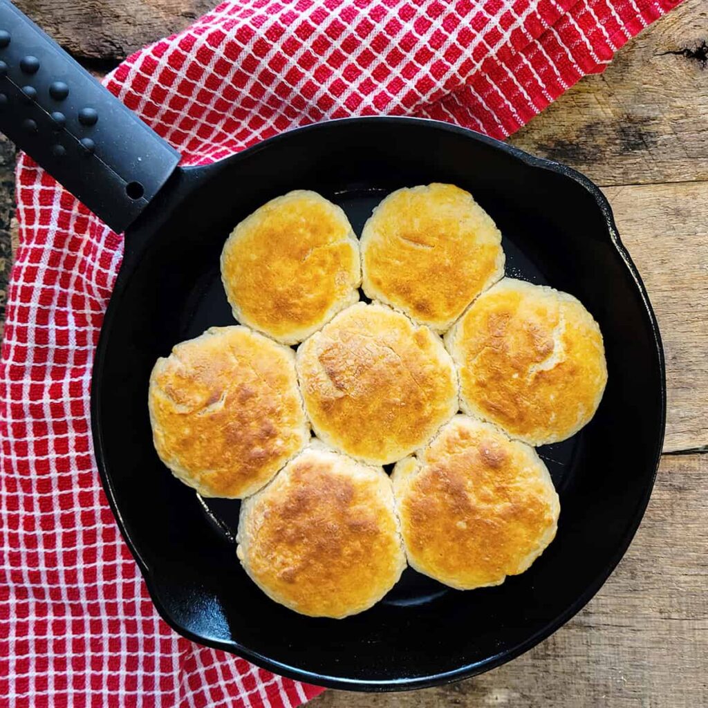 Baked buttermilk biscuits in a cast iron skillet on a wooden board.