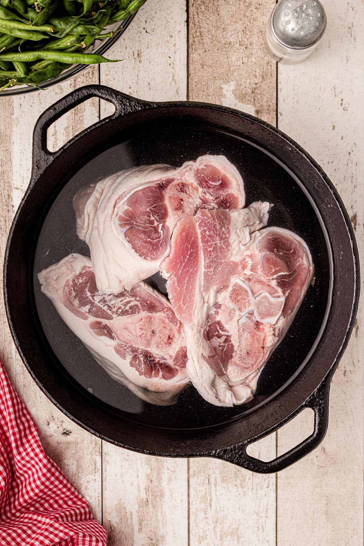 Meaty ham hocks in water in a cast iron pot.