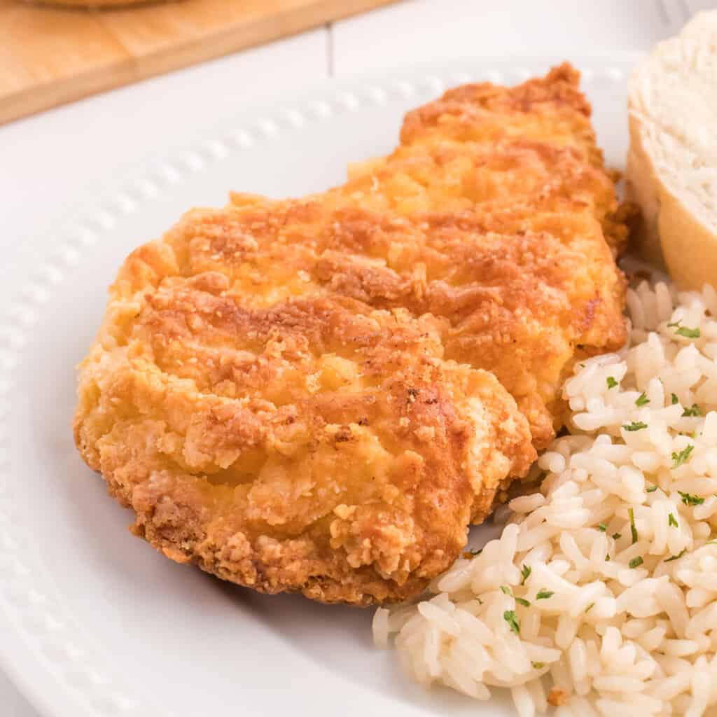 Finished chicken breast on a white plate with rice and roll on the side.