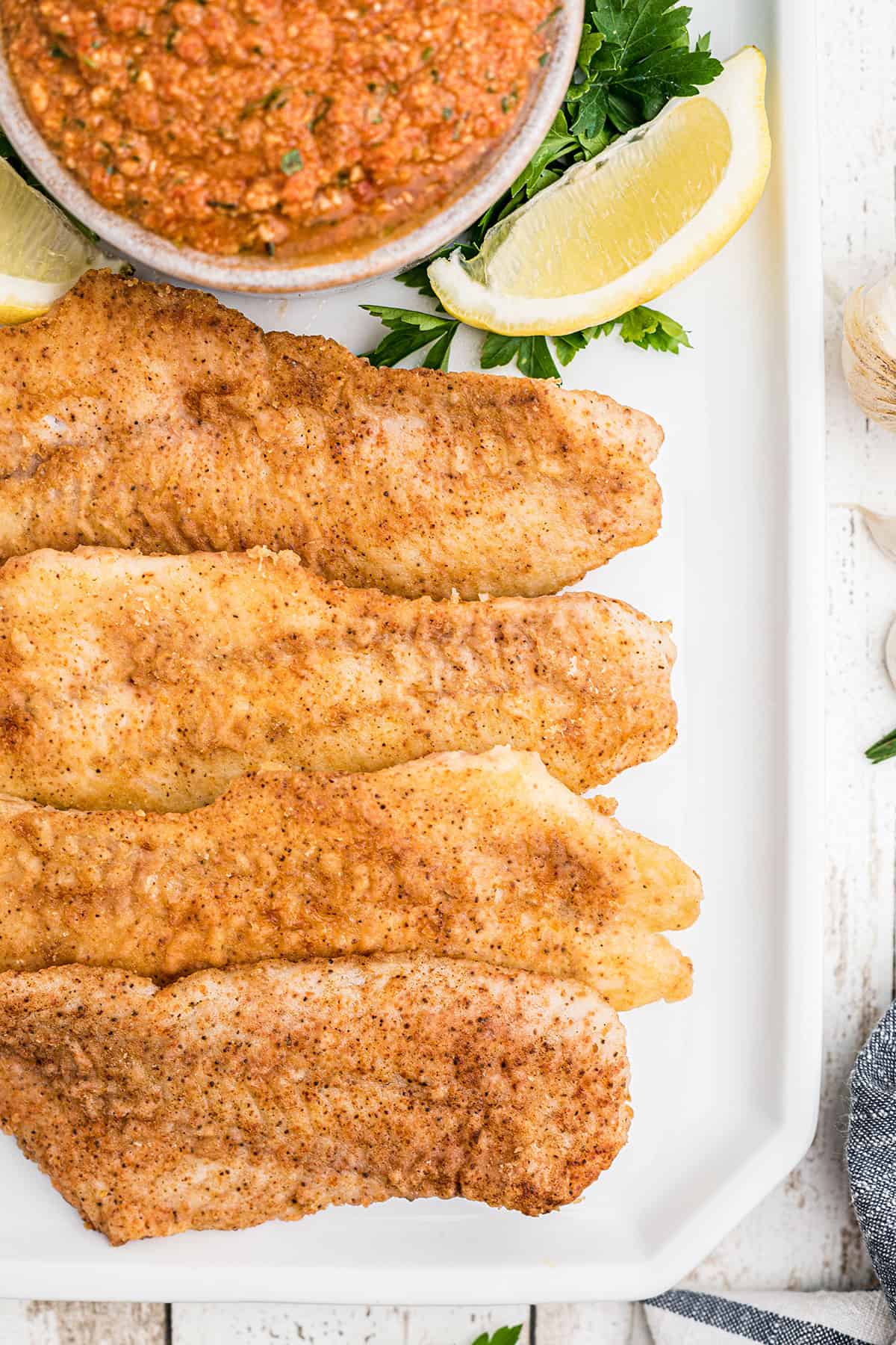 Fish fillets plated with lemon wedges and a bowl of romesco sauce.