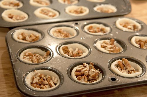 Adding chopped pecans to tart shells.