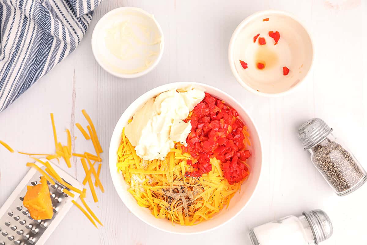 Grated cheese, mayo, and pimientos in a bowl.