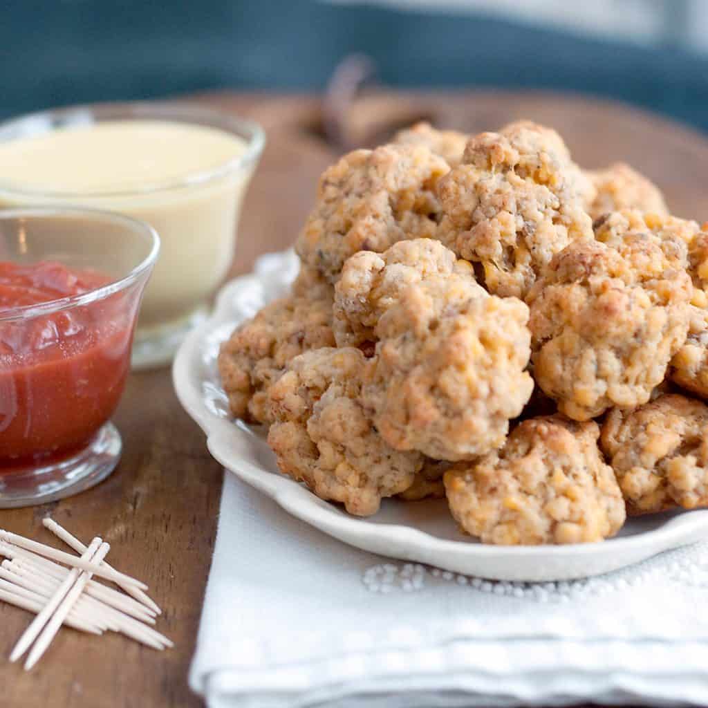 Sausage balls on a serving plate with two dipping sauces on bowls to the side.