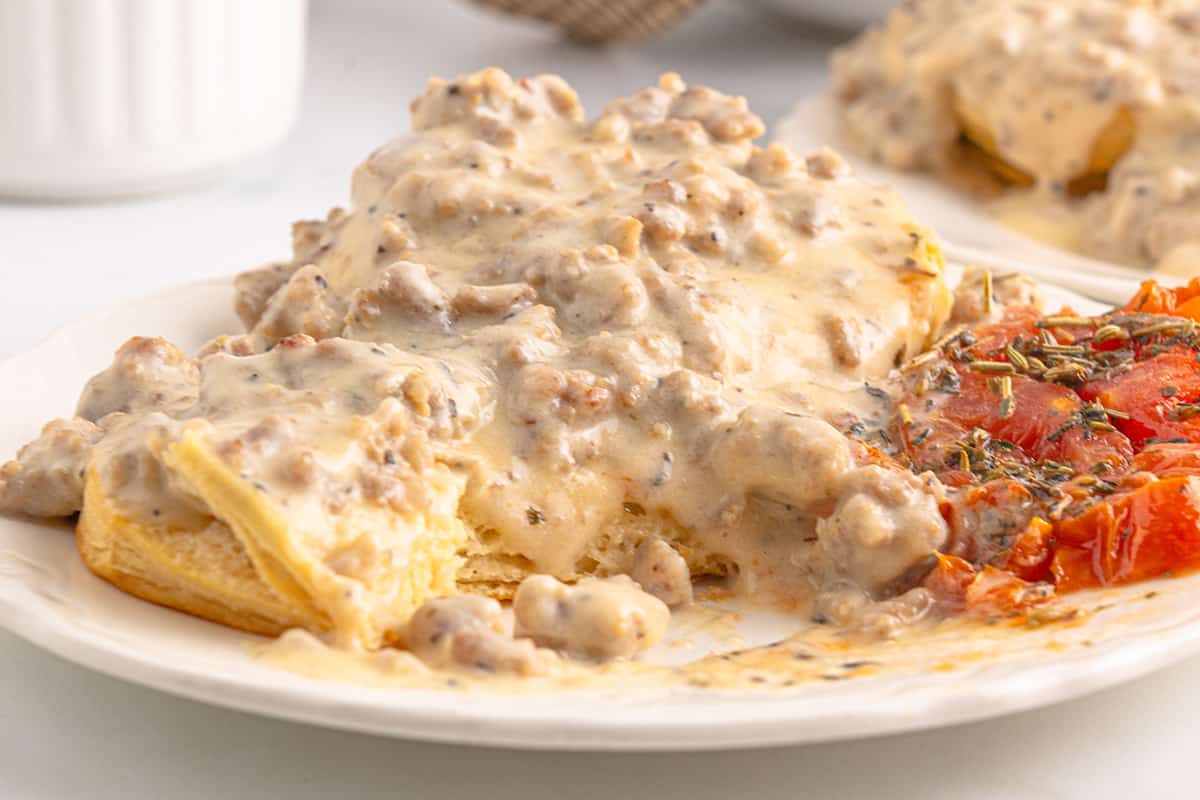 Sausage gravy and biscuits on a plate with baked tomatoes.