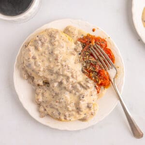 Sausage gravy and biscuits on a plate with baked tomatoes.