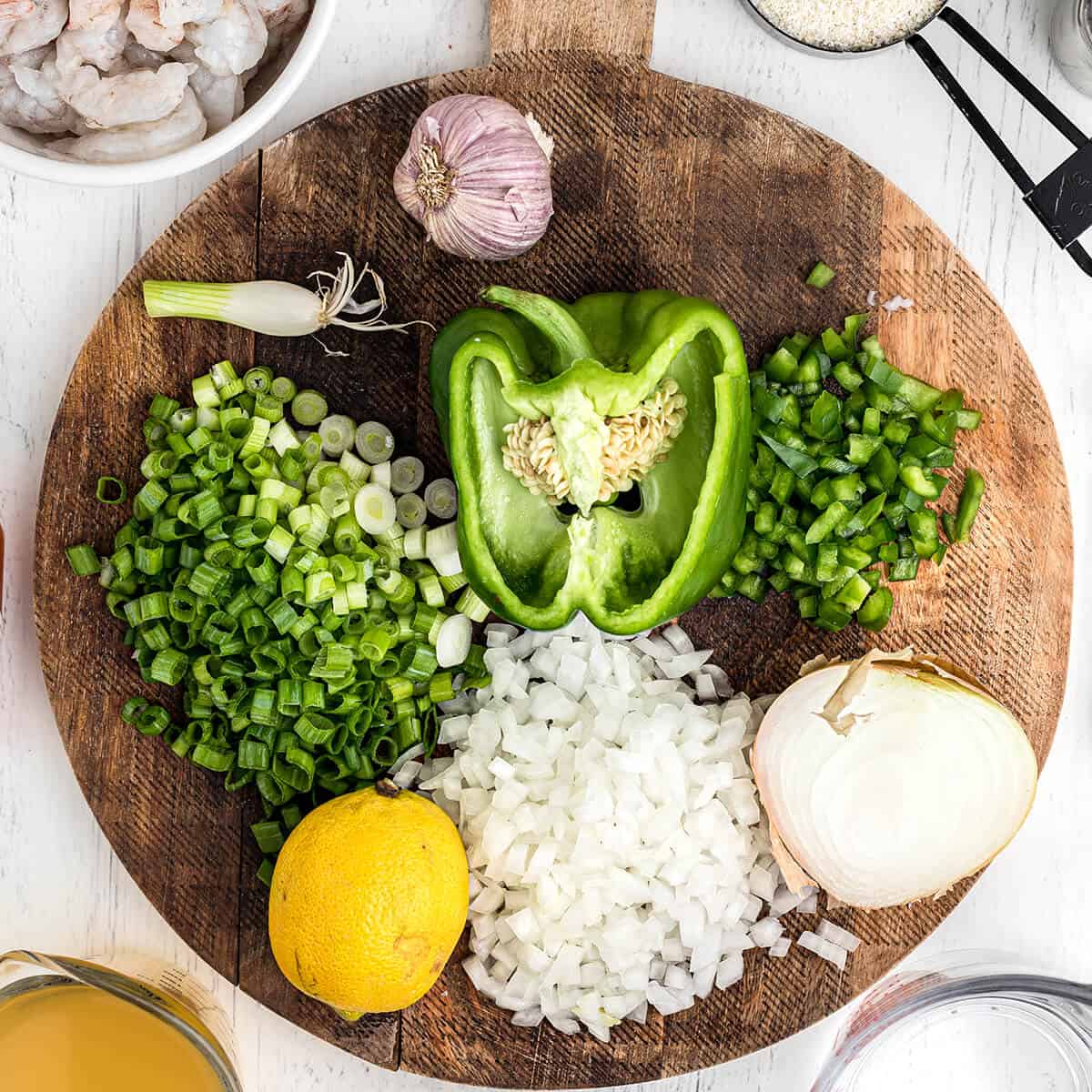 Peppers, onion, and garlic chopped on a wooden board.