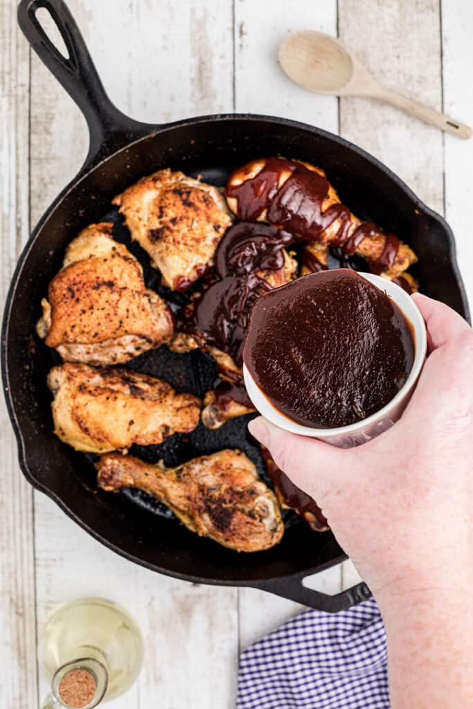 Pouring bbq sauce over chicken in a skillet.