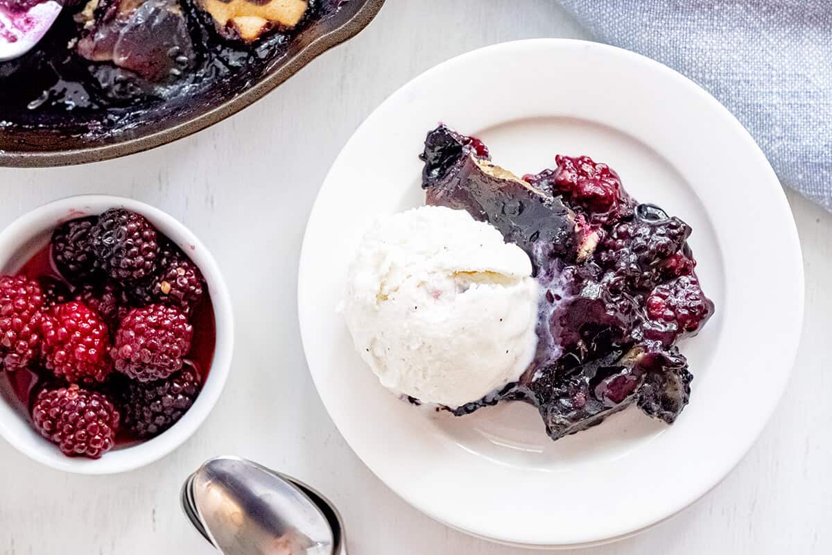 A serving of blackberry cobbler with ice cream on a white plate.