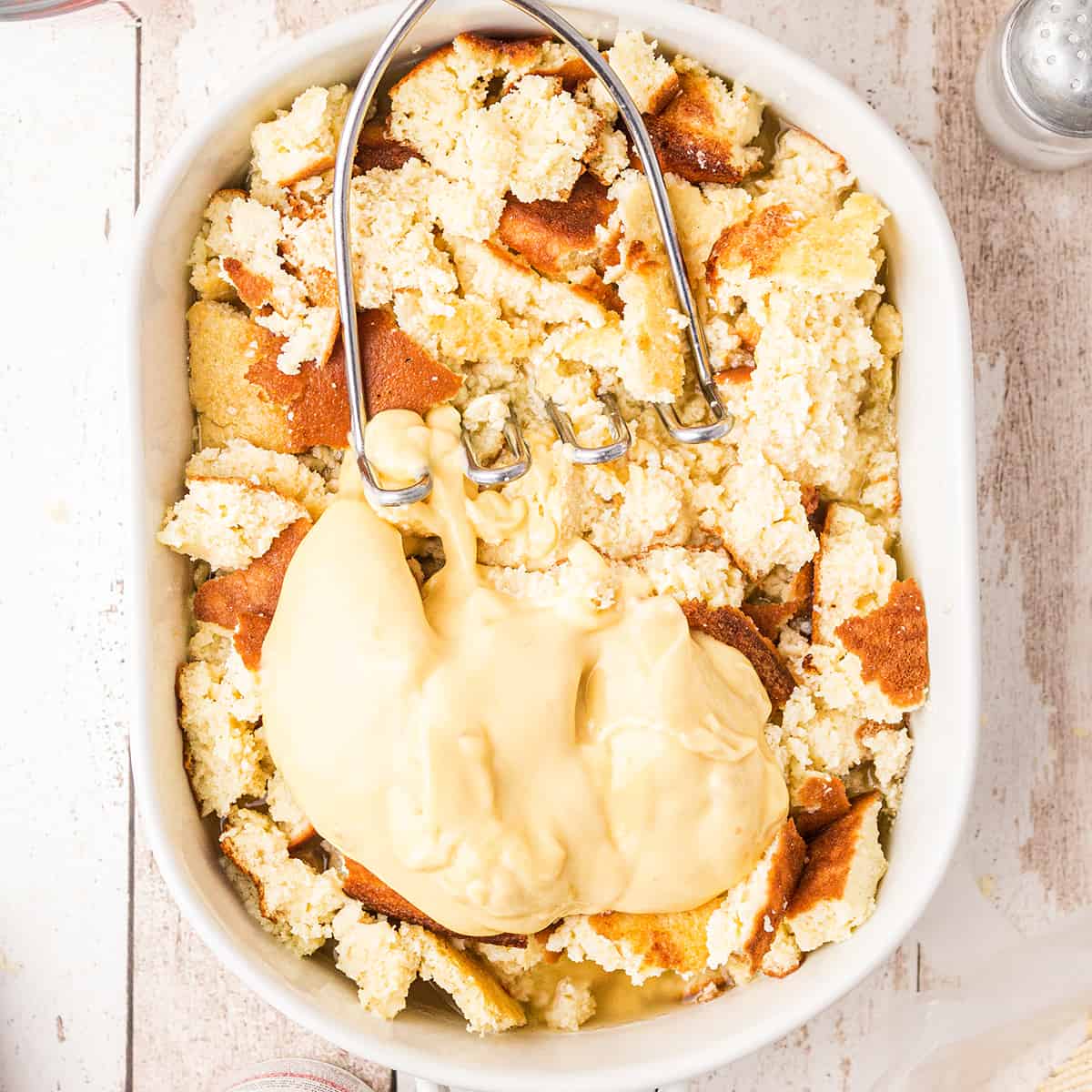 Crumbled egg bread and cream of chicken soup in a baking dish with a potato masher.