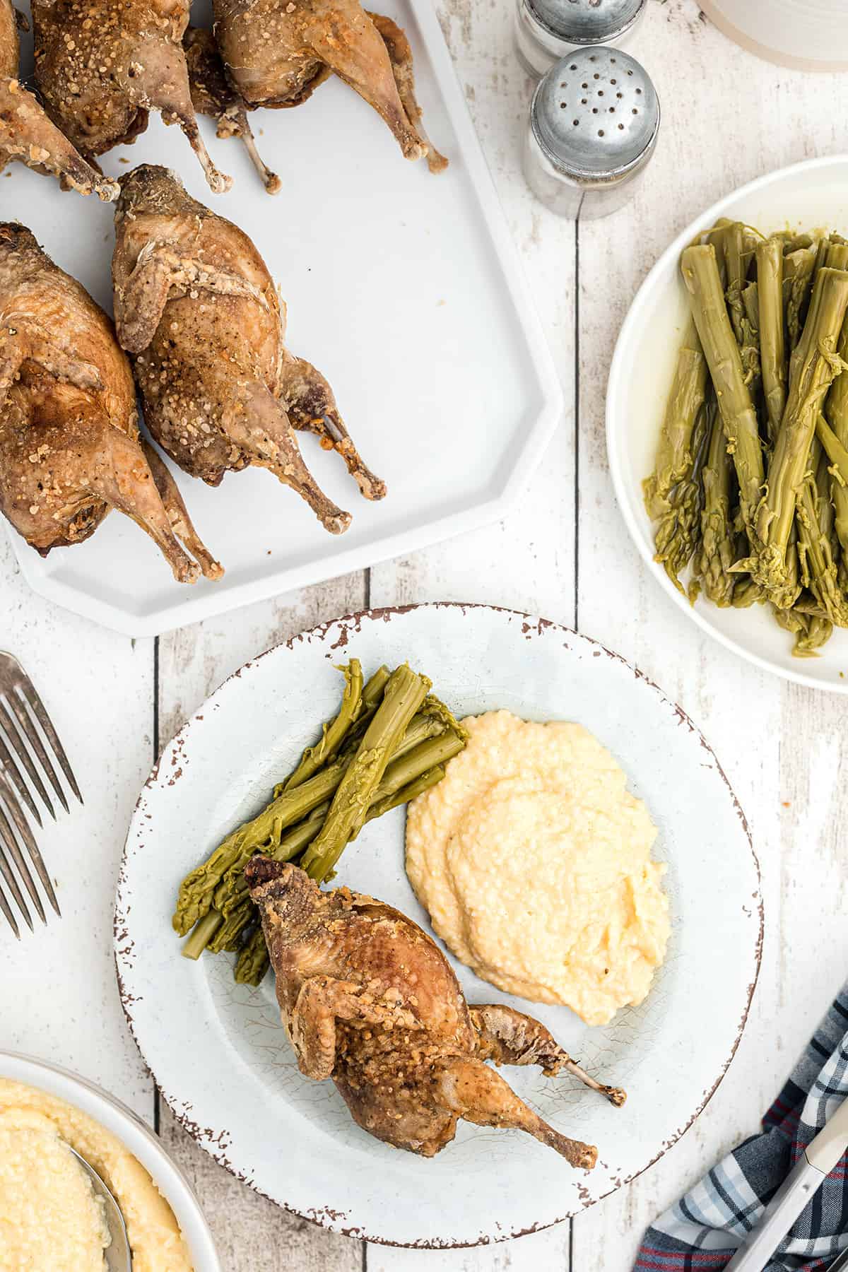 A serving of fried quail on a plate with cheese grits and asparagus.