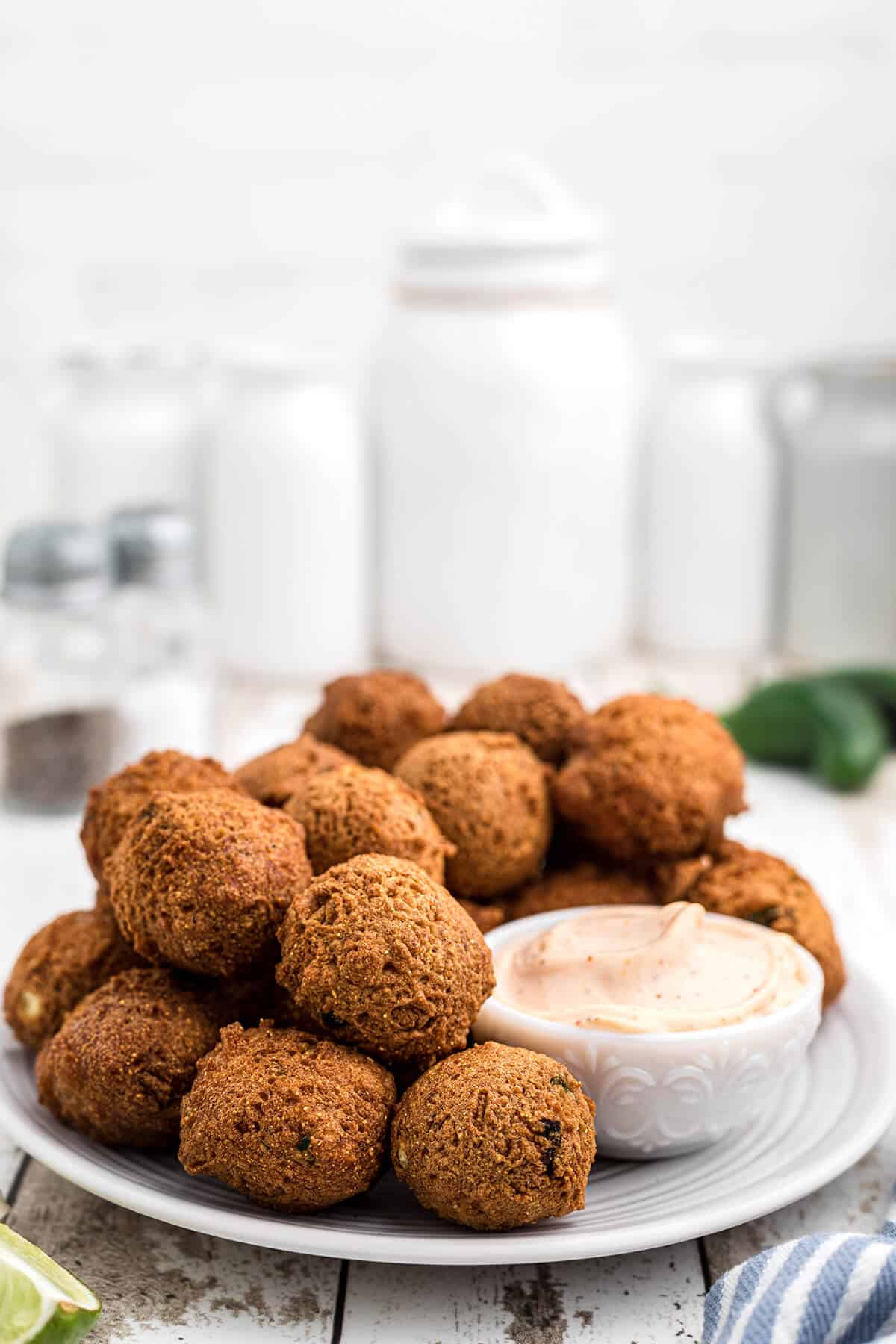 Finished hush puppies on a plate with dipping sauce on the side.