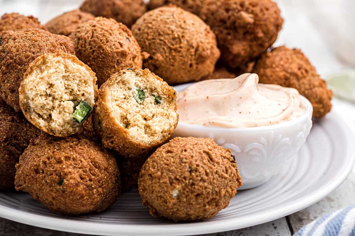 Finished hush puppies on a plate with dipping sauce on the side.