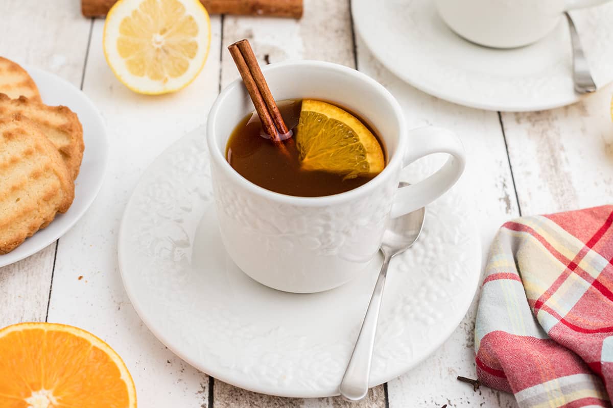 A cup of spiced tea with a lemon slice and a cinnamon stick in the cup.