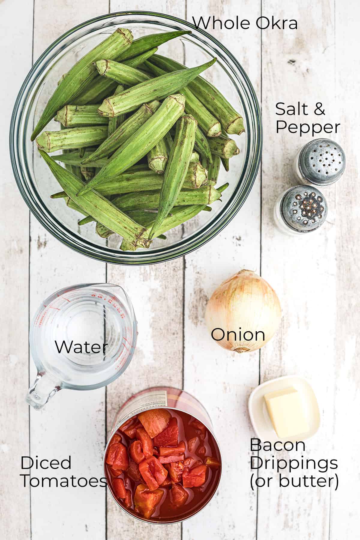 Whole okra, tomatoes, onion, butter, salt, pepper, and water on a table.