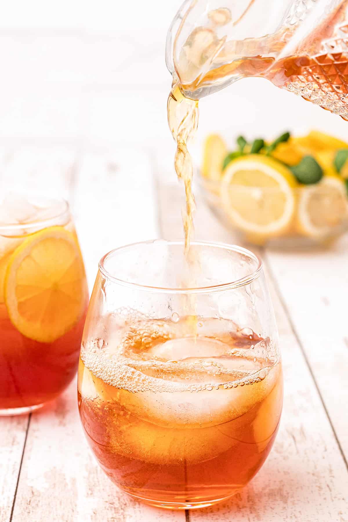 Tea being poured from a pitcher into a glass with ice.